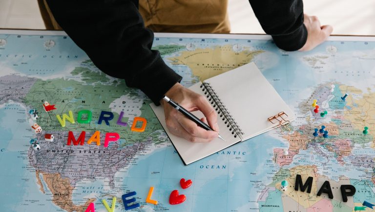 Person Writing in a Journal on Top of a World Map